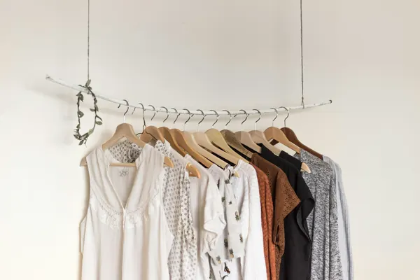 Light, neutral garments hanging on a minimal clothes rail in a bright room